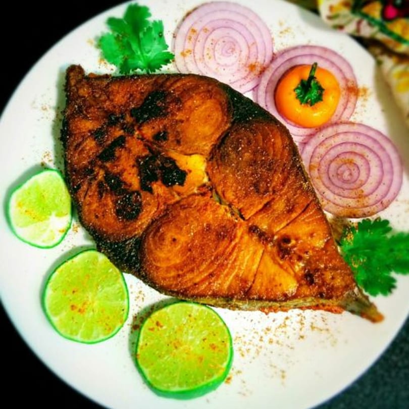 Avinya Indian Cuisine's fried fish steak, garnished with lime, red onion, and cilantro on a white plate.