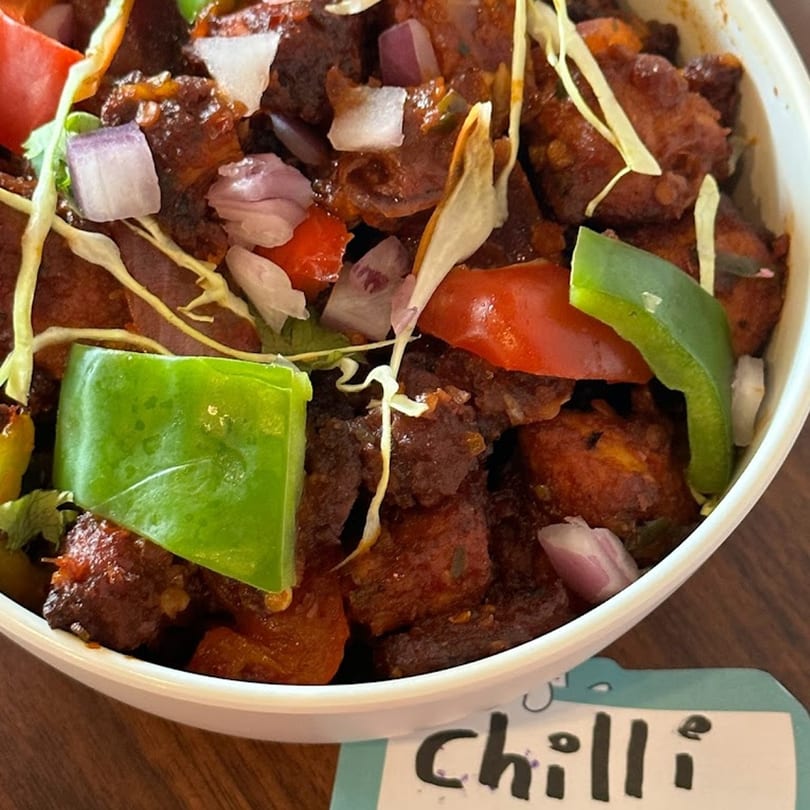 Close-up of Avinya Indian Cuisine's Chilli Chicken, garnished with bell peppers, onions, and cabbage.